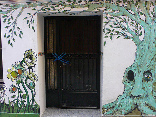 Dibujo de un árbol y flores en una pared de una casa, al lado de una puerta