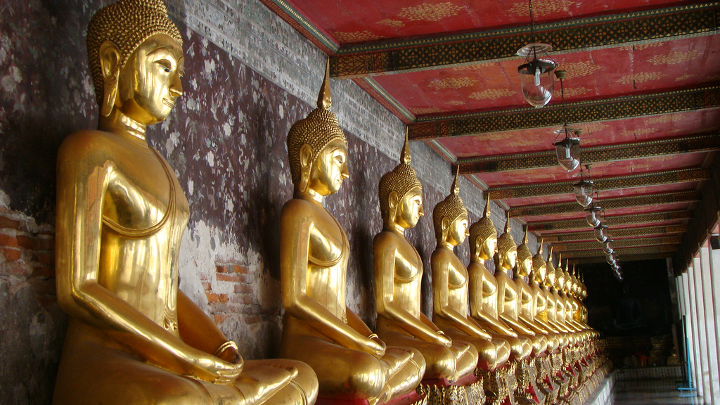 templo de Bangkok con una fila larga de esculturas de Budas dorados uno al lado del otro apoyados en una pared de un pasillo