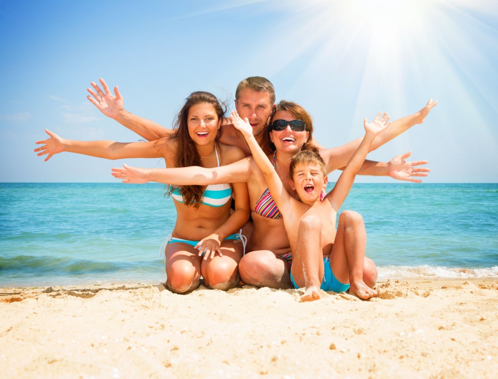 una familia de 4 personas, pare, madre, hija adolescente e hijo menor, abriendo los brazos y sonriendo en la playa