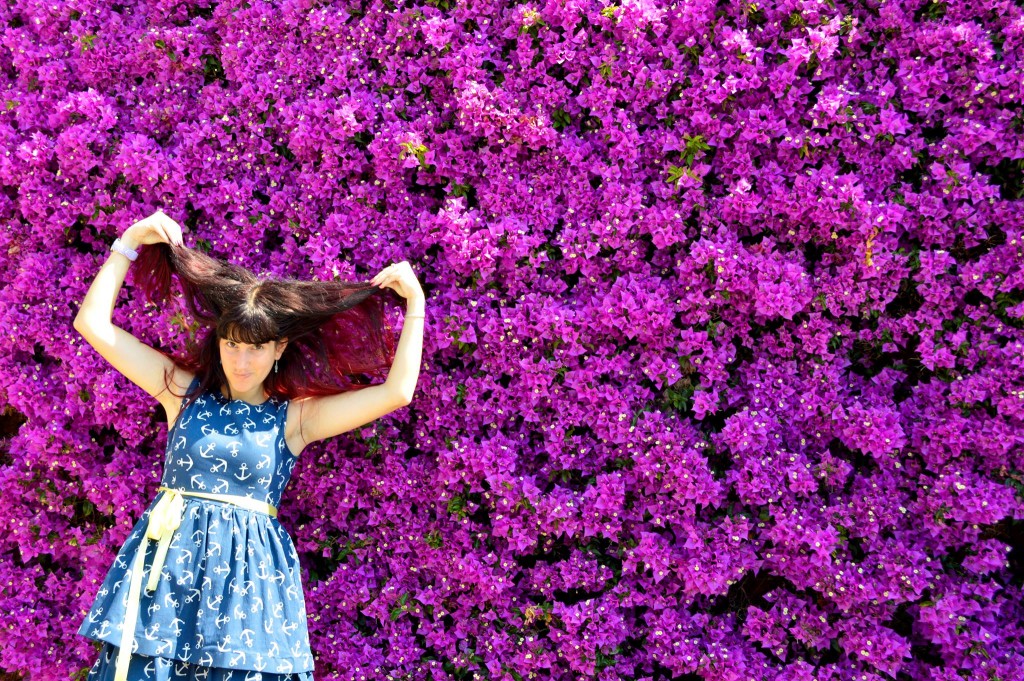 chica agarrandose los pelos de forma alegre, de fondo una pared de flores violetas