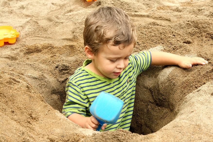niño dentro de un pozo en la arena con una pala de plástico