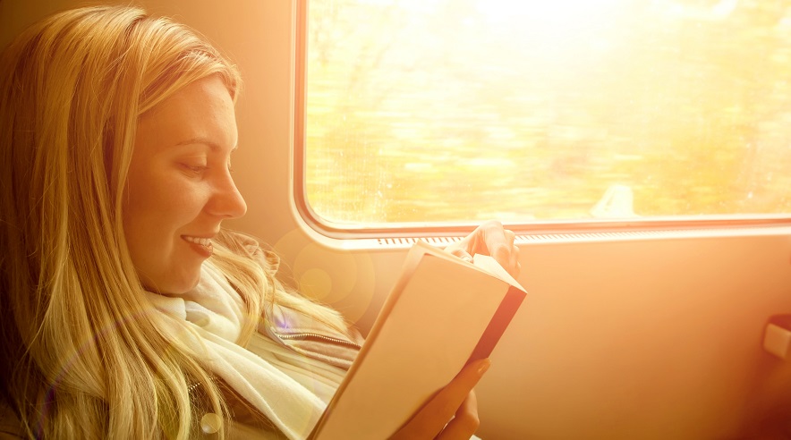 Un achica leyendo un libro al lado de la ventana de un tren