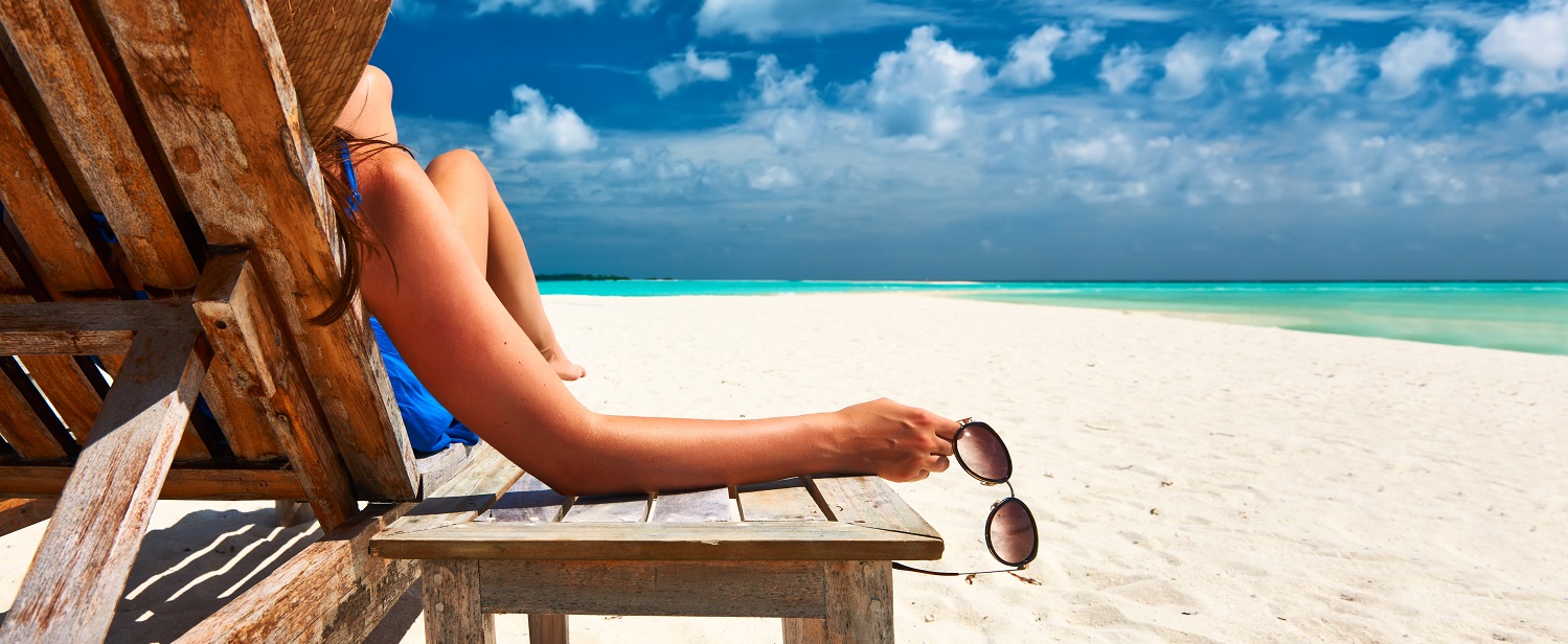 Señora sentada en una hamaca de madera frente a una playa con arena blanca y agua cristalina